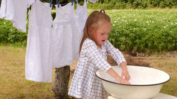 一个穿着格子衣服的女孩在后院用手在盆里洗衣服花园里树下晾衣绳上晾晒着雪白的纺织品
