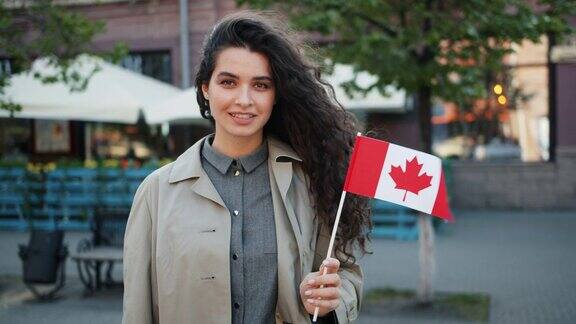 一个漂亮的年轻女士举着加拿大国旗在街上微笑的肖像