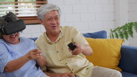 微笑的亚洲老年夫妇玩游戏玩得开心在家里使用虚拟现实坐在客厅的沙发上
