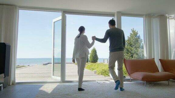 幸福的年轻夫妇手牵着手非常爱跑出他们的家到阳台与海边的景色