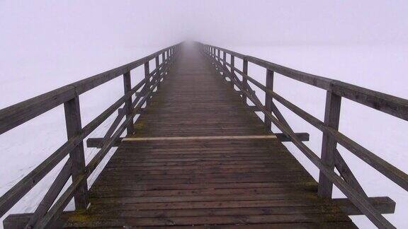 走在空旷的旧木桥上在清晨黑暗的雾中