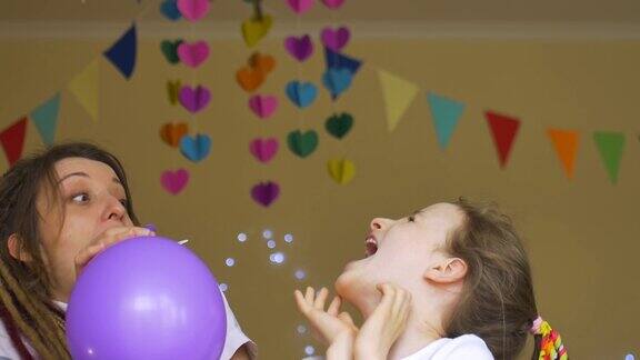 孩子的生日派对可爱的小女孩正在庆祝她的生日与年轻的母亲与发辫充气彩色气球在纸花环的背景在家里