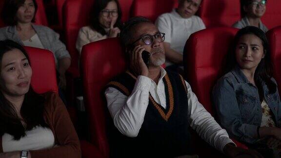 一位亚裔中国老人在电影院看电影时使用智能手机打扰她周围的观众