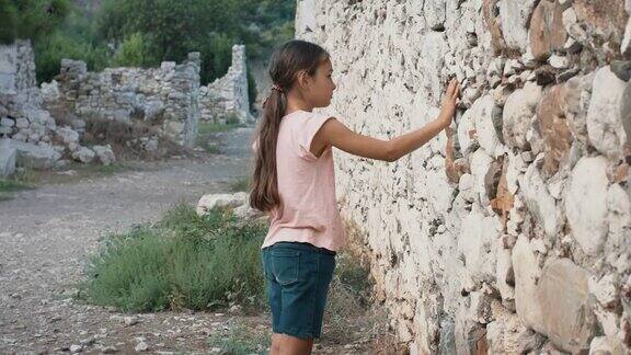 年轻的女孩触摸着古老的墙壁上的石头体贴的女孩触摸着旧墙