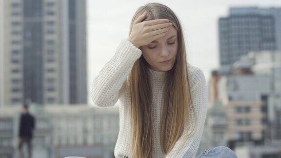 悲伤的年轻女子有发烧触摸额头和脸和叹息坐在城市广场上的病态白人女士的肖像医学