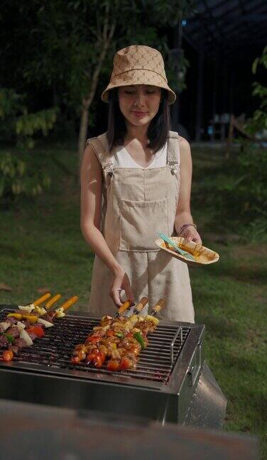 年轻的亚洲妇女烹饪烧烤串牛肉和猪肉与蔬菜烧烤在后院的木炭烧烤野餐时间