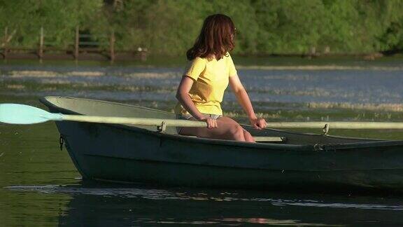 那女孩用桨操纵那艘旧船乘船在湖面上漫步Slowmotion