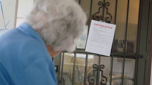 一位100岁的老妇人站在一户人家的前门上看着一张驱逐令