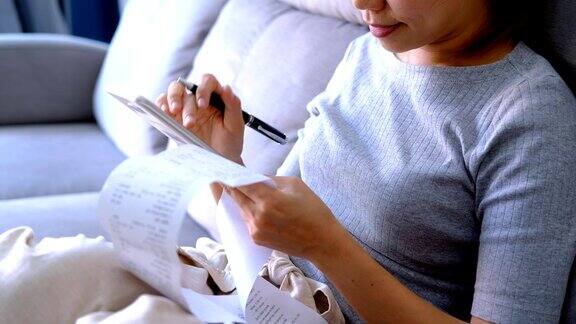 年轻女子在家里的客厅里查看账单使用智能手机和计算开支