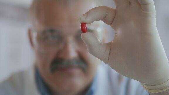 一位男性科学家手里拿着一颗红色的药丸近距离观察它的慢镜头
