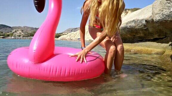 年轻苗条的女人享受大海和太阳走进水里与一个粉红色的充气火烈鸟