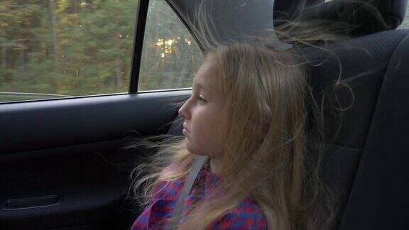 年轻美丽的女孩在冒险公路旅行车内风在她的头发很严肃的白人女孩道路速度驱动强风旅行秋天的日落背光灯日光