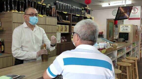 亚洲华人男性药剂师在中药店柜台协助一位活跃的高级顾客