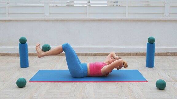 健身妇女做腹肌数百仰卧起坐接近膝盖腿弯曲在膝盖固定的运动球的手在头后的运动垫