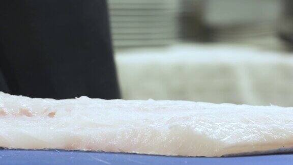 在餐馆的厨房里厨师将鳕鱼切成薄片我们只能看到厨师的手切生鱼-特写-烹饪和食物
