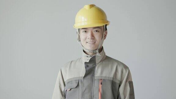 年轻的亚洲男工程师戴着头盔穿着工作服对着镜头微笑中国工人和工程师