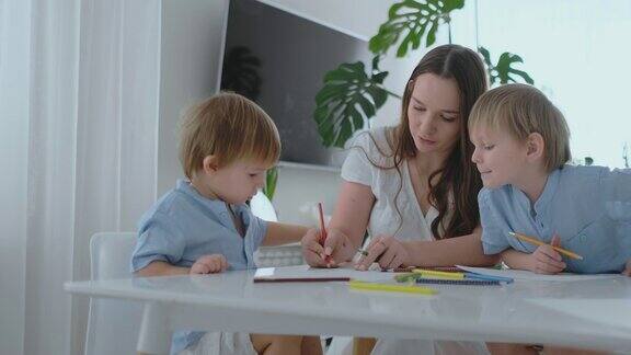 年轻的妈妈和两个2-4岁的儿子坐在客厅的桌子上用铅笔在boomega上画慢动作