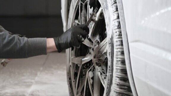 一名年轻人在自动洗车处用刷子清洗汽车边缘的表面
