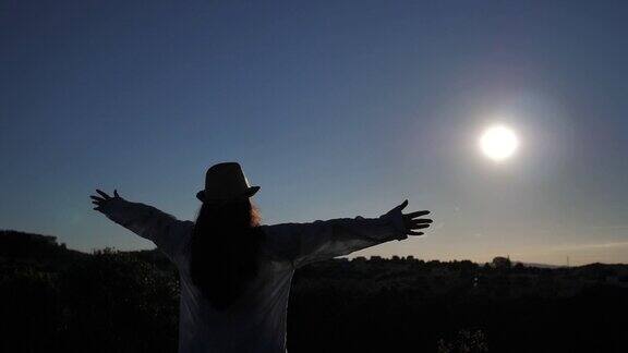 一个女人站在上面看着在黎明时分举起她的手向太阳