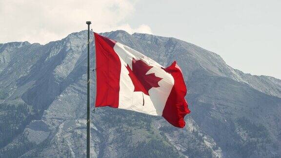 加拿大国旗在风中吹动的慢动作镜头与山在一个阳光明媚的日子的背景