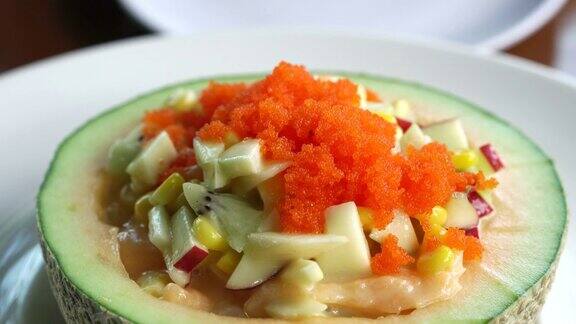 水果沙拉在哈密瓜碗用勺子舀西瓜、甜瓜、沙拉酱和鱼卵放在健康食品上