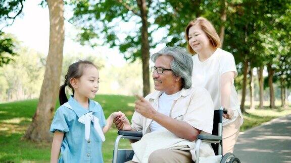 亚洲一家在公园度假放松爷爷坐在轮椅上慢动作