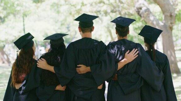 毕业典礼上站在一起的学生的后方一群成功的毕业生团结在一起戴着帽子穿着长袍获得了大学文凭证书感到很有成就感