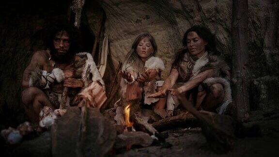 穿着兽皮的史前狩猎采集者部落晚上住在洞穴里尼安德特人或智人家庭试图在篝火取暖手在火上烹饪食物
