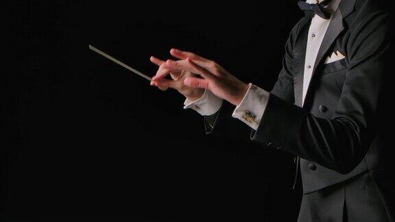 黑色背景下身穿西装的交响乐团指挥正在指挥指挥棒的移动用明显的手势指挥、指挥音乐表演近距离