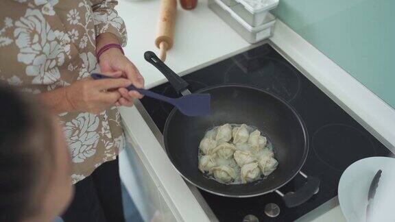 近距离的中国奶奶准备煮蒸汽中国饺子在烹饪锅在itchen