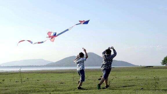快乐的两个小男孩带着风筝在草地上奔跑在夏日阳光明媚的大自然中慢动作