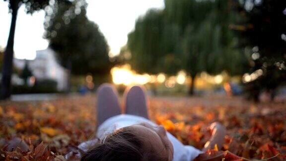 可爱的小女孩躺在夕阳下的落叶里