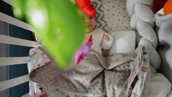 刚出生的小男孩躺在他的婴儿床上看着悬挂移动