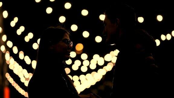 年轻的情侣亲吻剪影在一个夜晚的街道花环的背景
