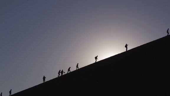 在纳米布-诺克鲁夫特国家公园内游客们在沙丘上的剪影中行走背景是旭日