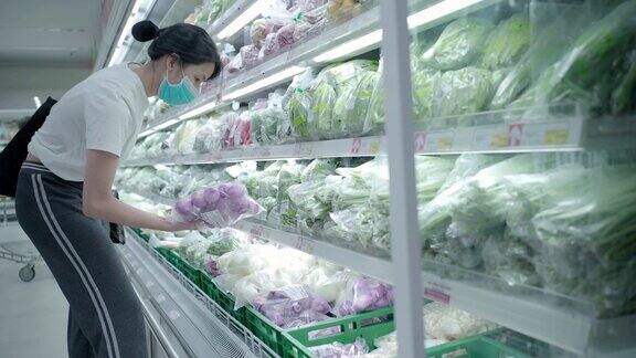 在新冠肺炎疫情封锁期间女性戴着医用口罩在杂货店买食物查看蔬菜货架、连锁超市储备食品供应