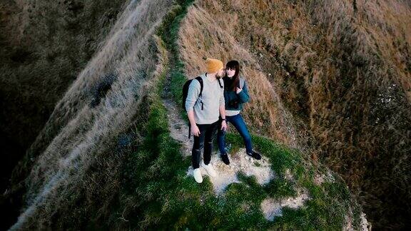 无人机绕着快乐的年轻新婚夫妇看史诗般的日落海景接吻在诺曼底海岸悬崖