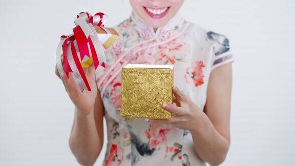 正面特写:中国亚洲妇女打开她手中的一个金色的大礼盒她从她的家人亲戚和朋友的新年快乐在中国的新年节日穿着旗袍白色的衣服