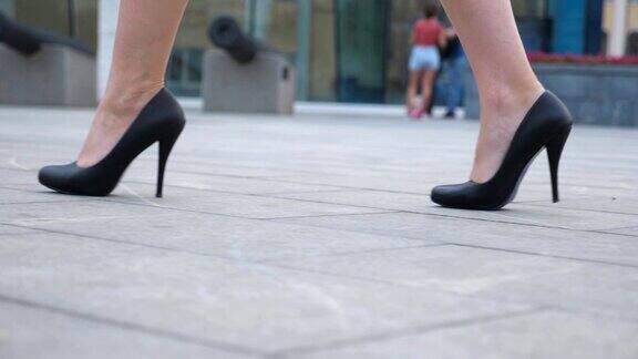 年轻女商人的脚穿着高跟鞋走在城市的街道上苗条女性的腿在黑色高跟鞋上走在城市女孩走着去上班低角度视角慢动作特写