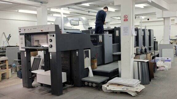 年轻的白人工人正在调整自动印刷机的工作