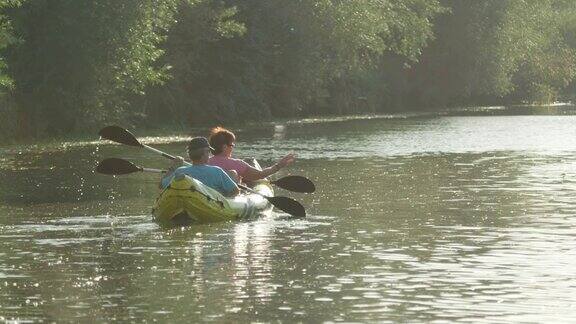 慢镜头:在阳光明媚的夏天一对夫妇在美丽平静的河边划皮艇度假