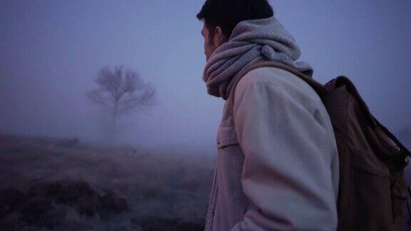 走在阴暗迷雾重重的田野上的男人慢镜头