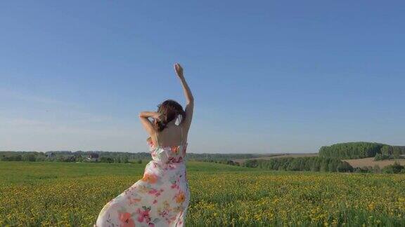 走在盛开的黄色田野上的漂亮女人举起了手臂