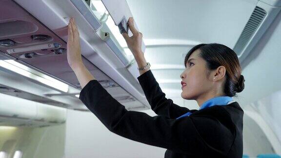 特写:美丽的亚洲空乘人员在制服关闭头顶的行李柜把乘客的行李在飞机里