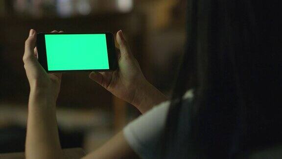少女在晚上使用绿色屏幕的风景模式的智能手机休闲的生活方式