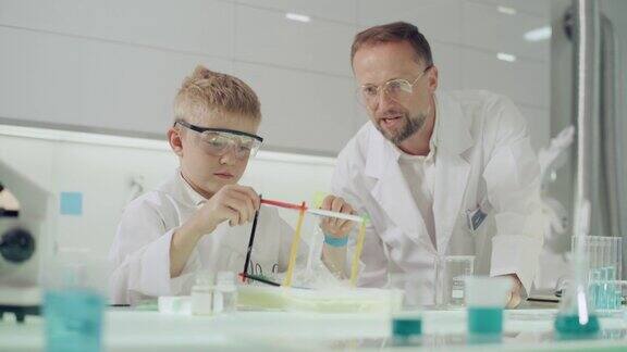男孩和他的老师一起做科学实验在实验室里玩得很开心用肥皂泡液研究表面张力