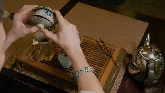 茶师将热水从茶壶倒入盖碗并在木桌上倒入绿茶