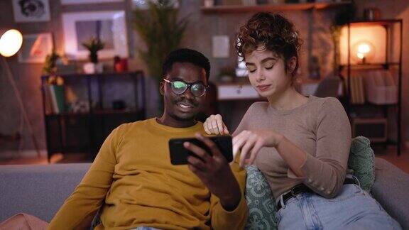 年轻漂亮的夫妇在智能手机上看在线娱乐视频