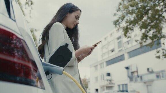 一位女士在给她的电动汽车充电时使用手机