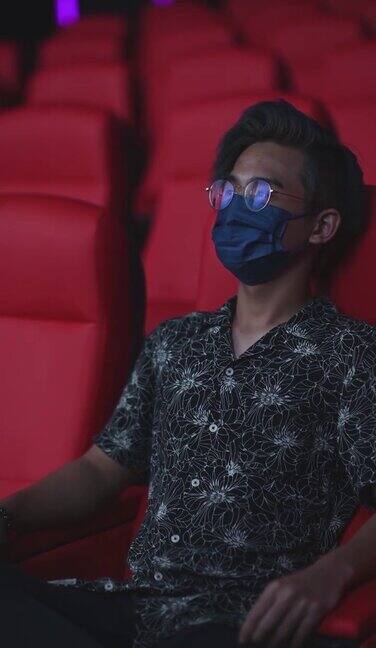 亚洲华人少年戴着口罩在电影院看电影呆若木鸡跷着二郎腿